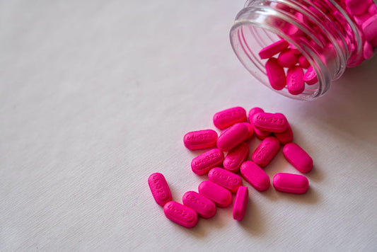 A spilled jar of vibrant pink pills representing trustworthy health supplements on a white background